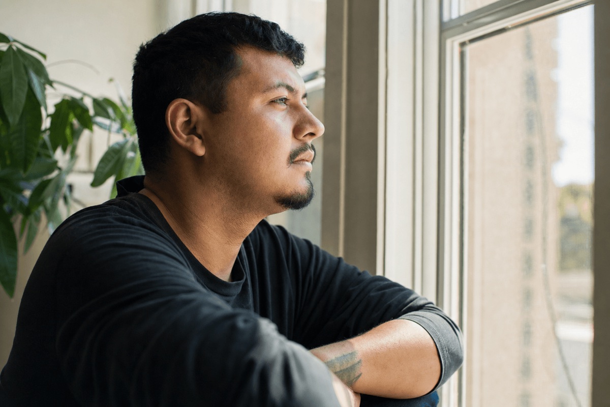 A person sitting thoughtfully by a window in soft daylight during a quiet moment of reflection
