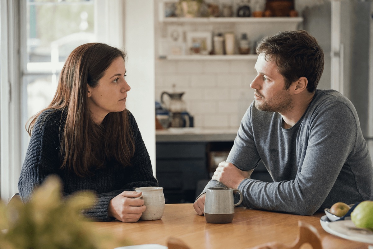 A couple sitting together at a kitchen table having a calm, serious conversation in soft morning light