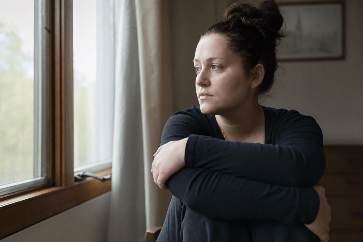 A person sitting quietly by a window in soft daylight, looking thoughtful and tense