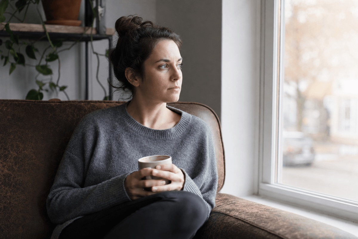 A person sitting alone by a sunlit window looking thoughtful and reflective during recovery