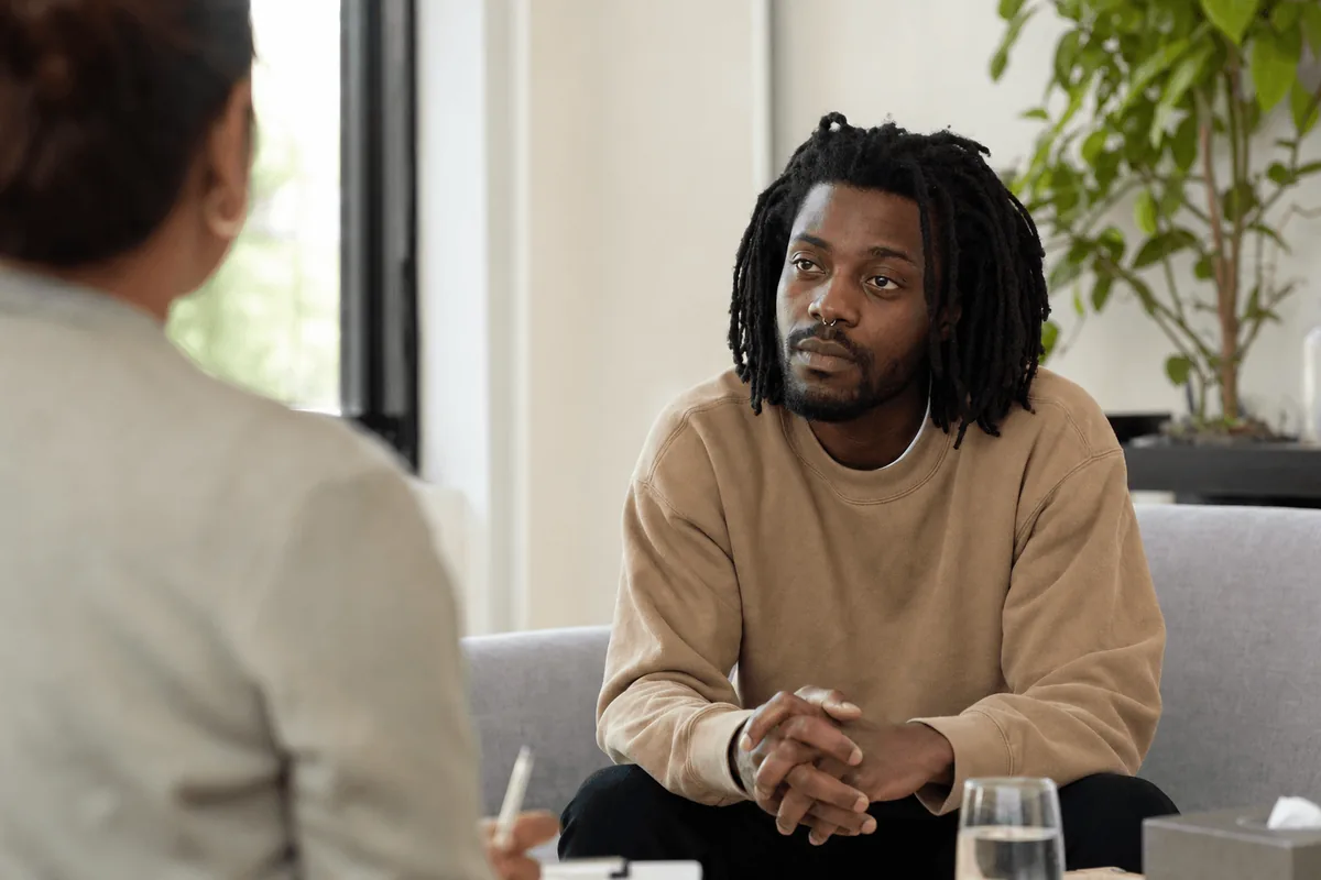A person sitting on a couch in a counseling session, listening thoughtfully in natural daylight