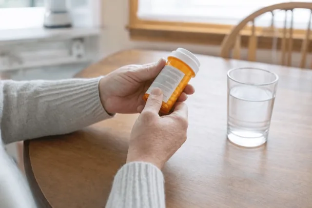A person reading the warning label on a prescription bottle at a kitchen table in soft daylight