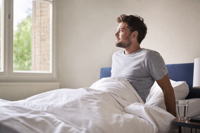 A person waking up rested by a sunlit window with a glass of water on the nightstand