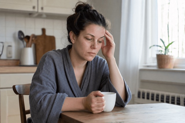 A person holding an empty coffee mug at a kitchen table in soft morning light