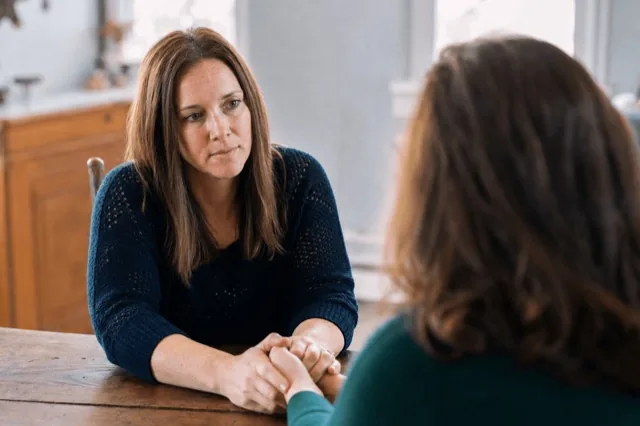 A woman holding the hand of a loved one across a table during a supportive conversation