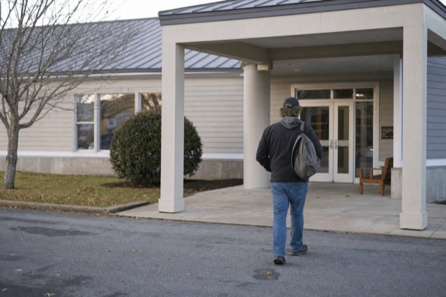 A person walking up to the entrance of a community addiction treatment clinic on a clear New England morning