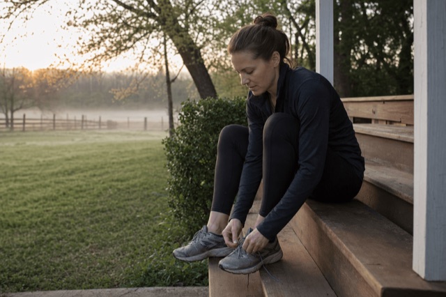 A person lacing up running shoes on a porch in the early morning before a run
