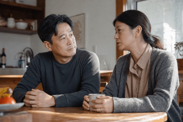 A married couple sitting together at a kitchen table having a calm, serious conversation in natural light