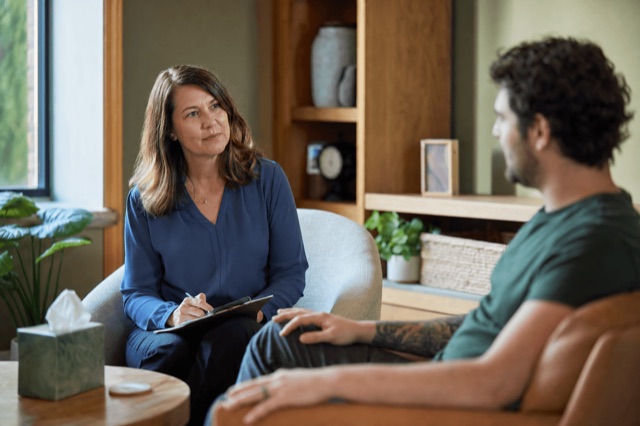 A therapist and client talking quietly during a one-on-one mental health session in a warm, calm office