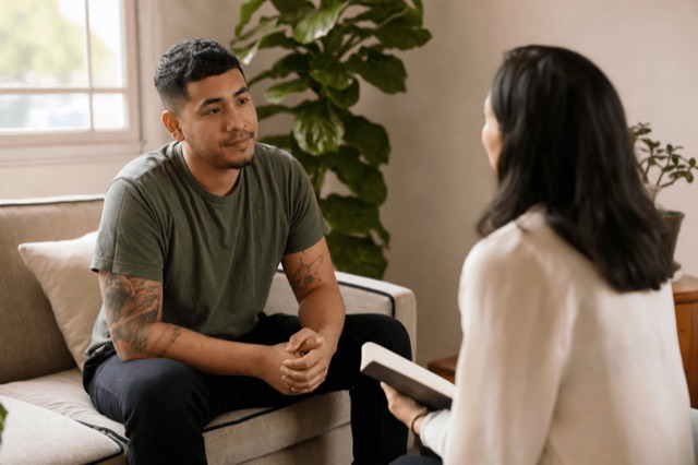 A person sitting with a supportive counselor during a recovery check-in in a calm, sunlit room