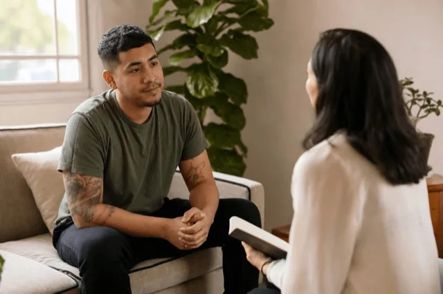 A person sitting with a supportive counselor during a recovery check-in in a calm, sunlit room