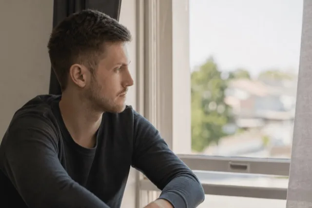 A person sitting quietly by a window in soft daylight, reflecting during a calm moment of recovery