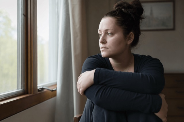 A person sitting quietly by a window in soft daylight, looking thoughtful and tense
