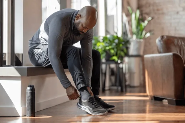 A person lacing running shoes by a sunlit window, part of a healthy daily routine in recovery