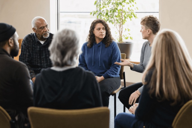 A small community recovery support group gathered in a bright room during a daytime meeting