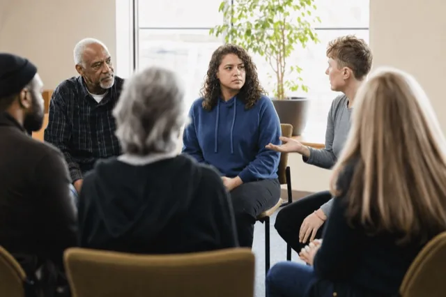 A small community recovery support group gathered in a bright room during a daytime meeting