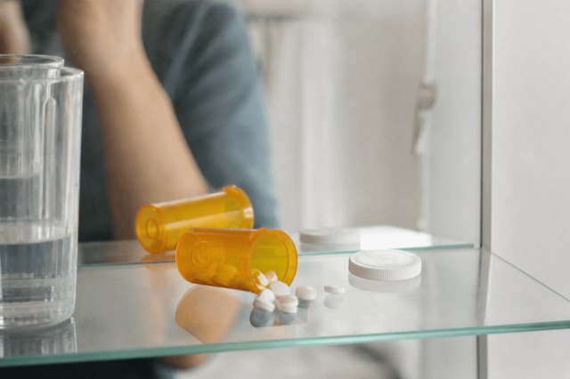 An open prescription pill bottle and loose tablets on a bathroom shelf in soft natural light