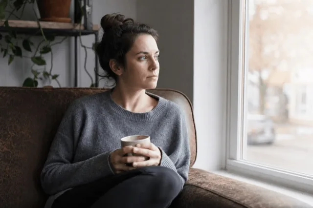 A person sitting alone by a sunlit window looking thoughtful and reflective during recovery