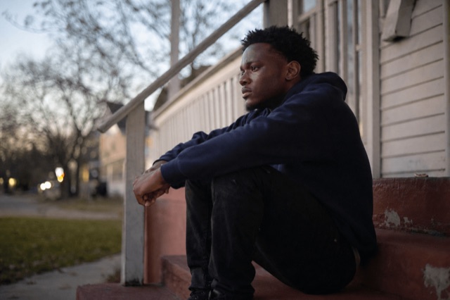 A young adult sitting alone on outdoor steps at dusk, looking thoughtful and weighed down