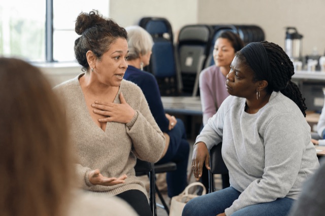 Two people in an honest, supportive conversation in a bright recovery group setting