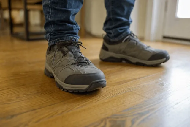Close-up of a person's feet in supportive shoes with custom insoles, standing on a wood floor